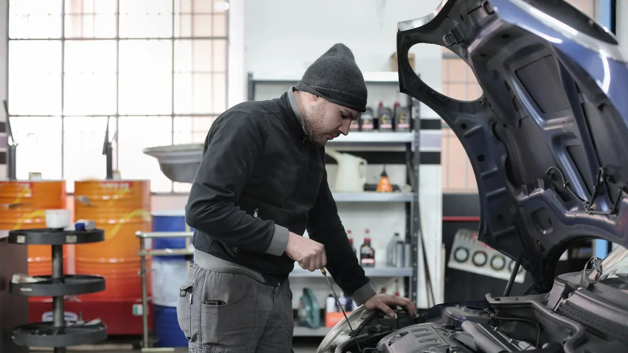Mécanicien auto contrôlant le niveau d’huile, capot ouvert, dans un garage.