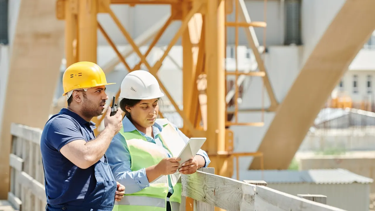 Deux professionnels du bâtiment consultent une tablette sur un chantier.