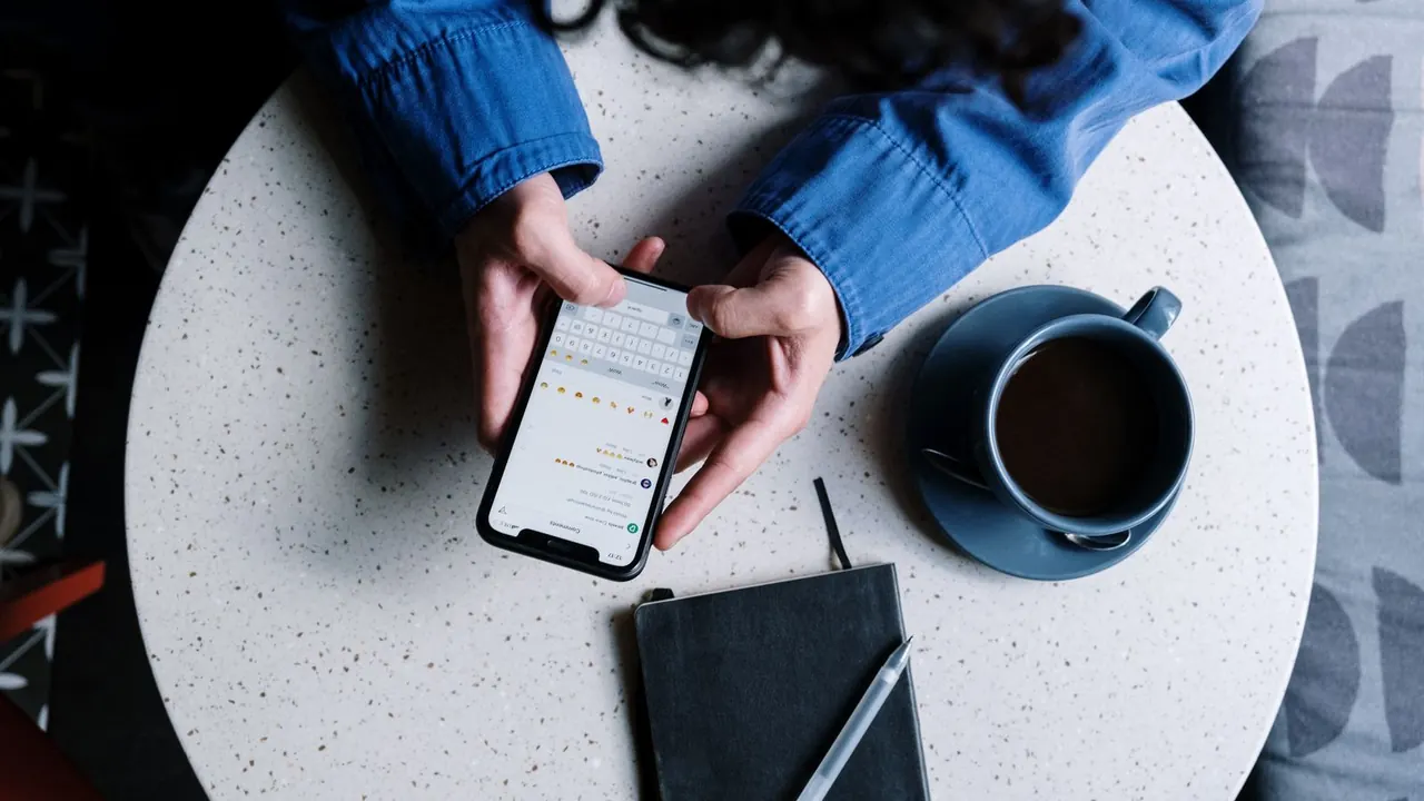 Personne envoyant un message depuis son smartphone, à une table, pour joindre un professionnel.