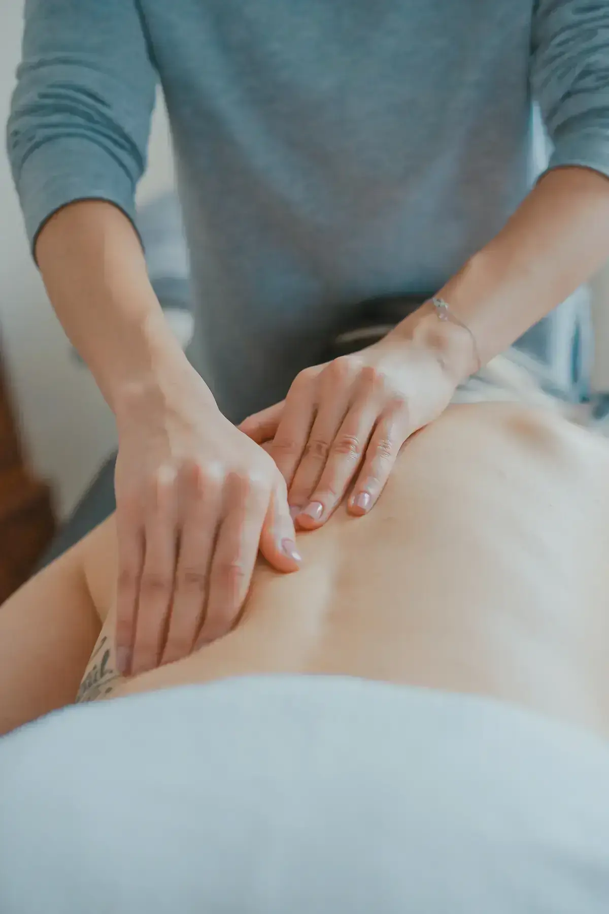 Mains d’une thérapeute posées avec douceur sur le dos d’une personne allongée
